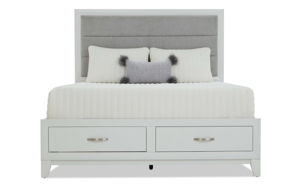Modern white wooden bed frame with built-in storage drawers, upholstered gray fabric headboard, and cream bedding with decorative pillows.