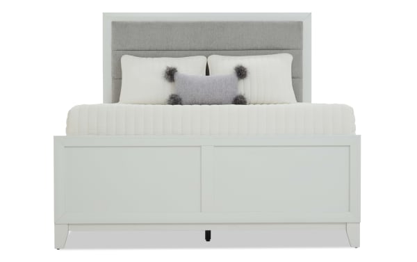 Queen-size bed with a light gray upholstered headboard, white panel footboard, and white bedding with decorative pillows, modern bedroom furniture.