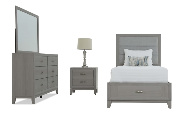 Gray wooden bedroom set with upholstered headboard, white bedding, matching dresser with mirror, and nightstand with lamp, modern style.