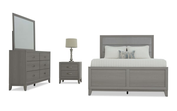 Modern gray wooden bedroom set with upholstered headboard, includes king bed, two-drawer nightstand with lamp, and six-drawer dresser with mirror.