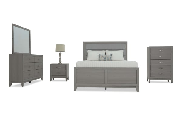 Gray wood bedroom set with upholstered panel bed, six-drawer dresser with mirror, two-drawer nightstand with lamp, and five-drawer chest, modern style.