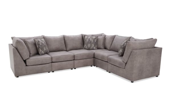 Large L-shaped sectional sofa upholstered in soft taupe fabric with thick cushions, angled armrests, and patterned accent pillows for modern living rooms.