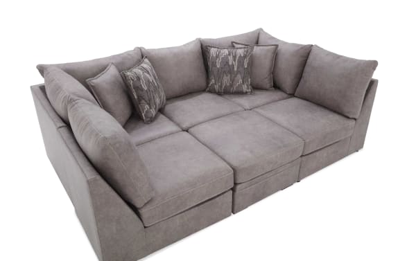 Modern sectional sofa in soft gray fabric upholstery with plush cushions and patterned throw pillows, designed for comfortable living room seating.