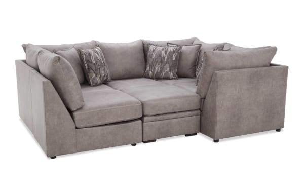 Modern sectional sofa in soft gray fabric with plush cushions and patterned throw pillows, featuring a contemporary design and clean lines.