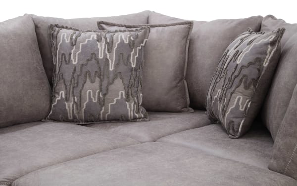 Section of a gray microfiber sectional sofa with plush cushions and two decorative throw pillows featuring textured abstract patterns in shades of gray and beige.