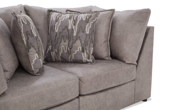 Section of a modern gray fabric sectional sofa with textured gray and taupe decorative throw pillows, featuring plush cushions and clean stitching.