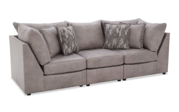 Modern three-seater sofa in soft gray microfiber fabric with plush cushions and patterned accent pillows, ideal for contemporary living rooms.