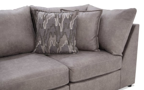 Section of a modern gray fabric sectional sofa with plush cushions and a decorative patterned throw pillow, showcasing soft texture and contemporary design.