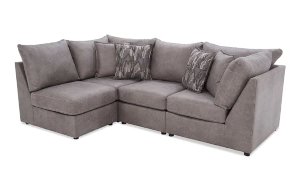 Modern L-shaped sectional sofa upholstered in soft gray fabric with plush cushions and patterned throw pillows, ideal for living room seating.