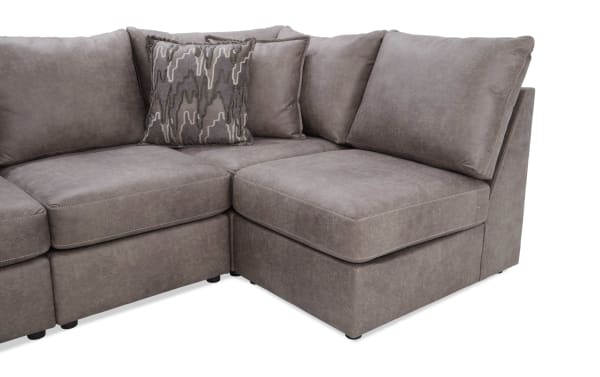 Section of a modern gray fabric sectional sofa with plush cushions and a decorative patterned throw pillow, showcasing corner seating.