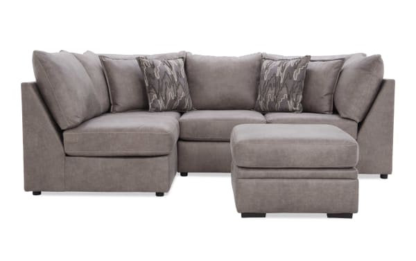 Modern L-shaped sectional sofa in taupe microfiber fabric with matching ottoman and patterned accent pillows, ideal for living room seating.