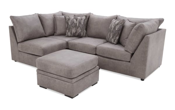 Modern gray fabric sectional sofa with matching ottoman, featuring plush cushions and decorative patterned throw pillows, ideal for living room seating.