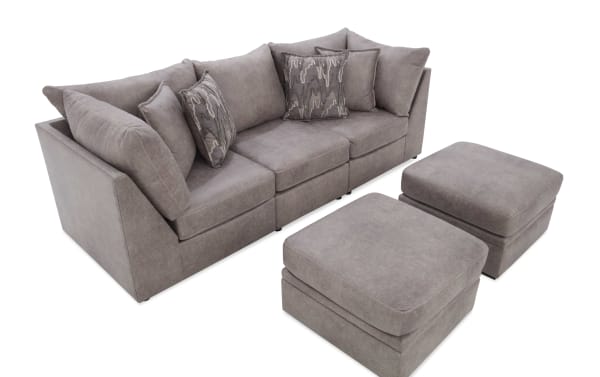 Modern gray fabric sectional sofa with three seat cushions, matching ottomans, and decorative pillows, ideal for contemporary living rooms.