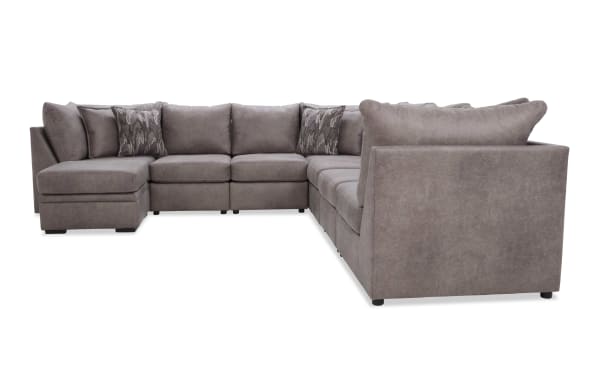 Large L-shaped sectional sofa in soft gray fabric with plush cushions and patterned accent pillows, designed for spacious living rooms.