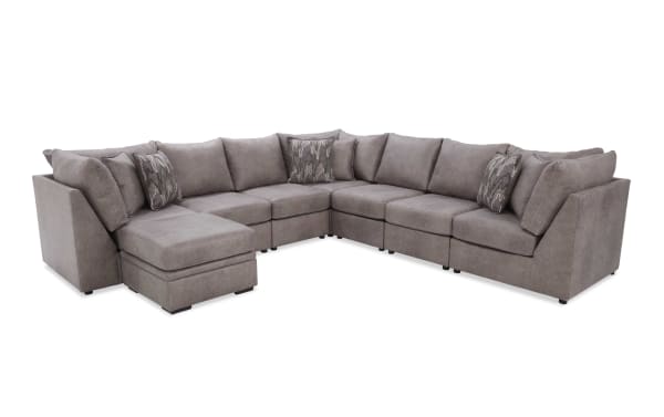 Large L-shaped sectional sofa in soft gray fabric with plush cushions and patterned accent pillows, ideal for modern living rooms.