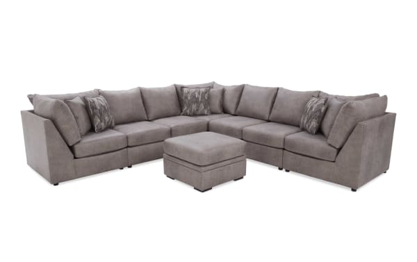 Modern sectional sofa set in soft gray fabric with plush cushions, patterned throw pillows, and matching ottoman, ideal for living room seating.