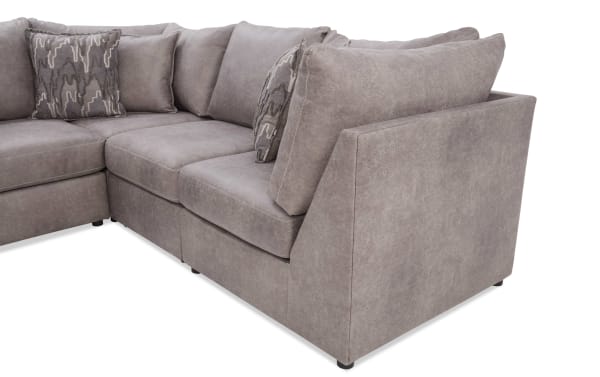 Section of a modern L-shaped sectional sofa in taupe microfiber fabric with plush cushions and patterned accent pillows, ideal for living room seating.