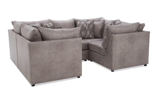 Sectional corner sofa upholstered in soft gray fabric with plush cushions and patterned throw pillows, ideal for modern living rooms.