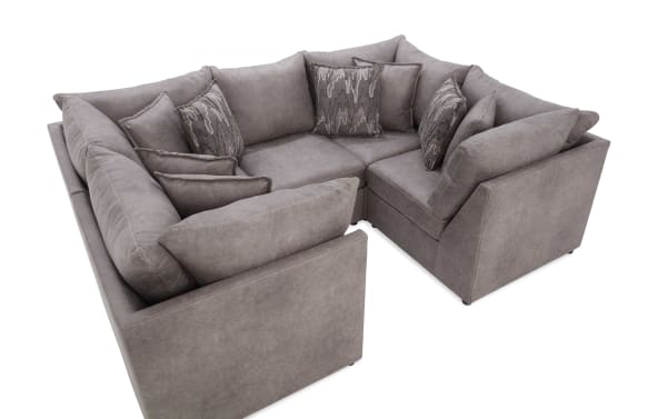 Modern L-shaped sectional sofa in soft gray fabric with multiple patterned and solid throw pillows, featuring plush cushions and a sleek design.