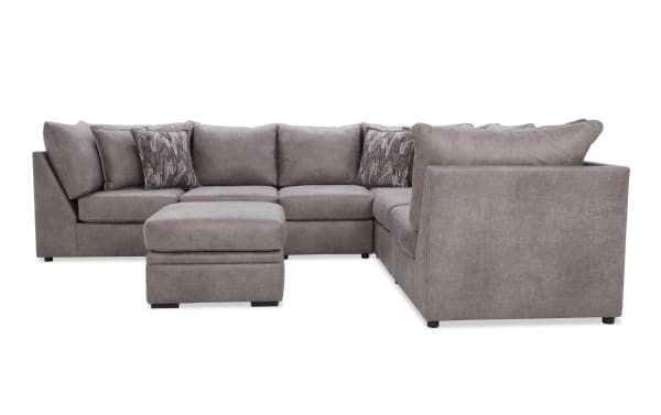 Gray sectional sofa with plush cushions and matching ottoman, featuring a modern design and soft fabric upholstery, ideal for living room seating.