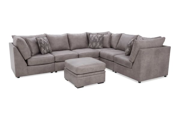 Modern gray fabric sectional sofa with plush cushions, patterned throw pillows, and matching ottoman, ideal for living room seating.