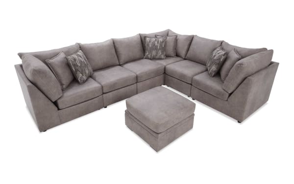 Gray sectional sofa with matching ottoman, featuring plush cushions and patterned throw pillows, ideal for modern living rooms.