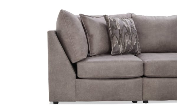 Section of a modern gray fabric sectional sofa with angled armrest, plush cushions, and a decorative patterned throw pillow, showcasing contemporary living room furniture design.
