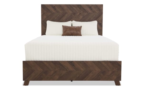King-size bed with dark brown chevron-patterned wooden frame and headboard, featuring white quilted bedding and a small brown leather accent pillow.