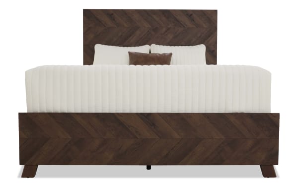 King-size bed with dark brown chevron-patterned wooden frame and headboard, featuring white ribbed bedding and a small brown accent pillow.
