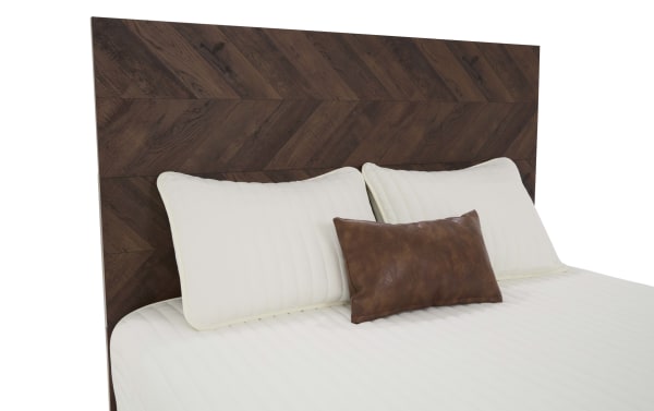 Queen bed with a dark brown chevron-patterned wooden headboard, white quilted bedding, two large white pillows, and one small brown leather accent pillow.