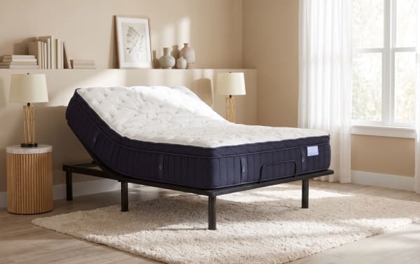 Adjustable bed frame with a thick, plush mattress featuring a white quilted top and dark navy sides, set in a bright, modern bedroom.