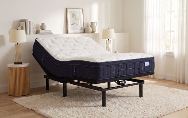 Adjustable split king mattress with white quilted top and navy blue sides on black metal frame, set in a modern bedroom with beige decor.