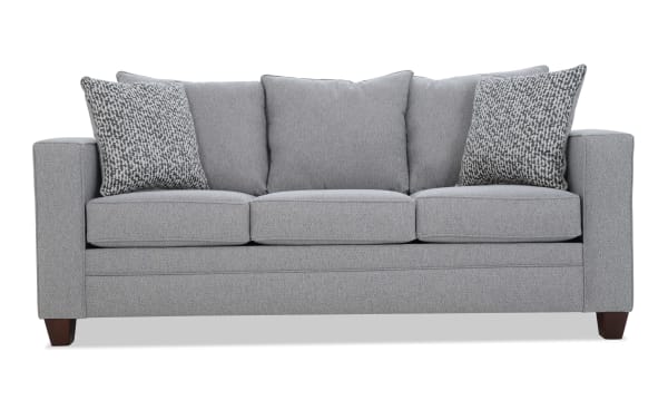 Gray fabric three-seater sofa with square arms, wooden legs, and five cushions including two patterned accent pillows, modern style.