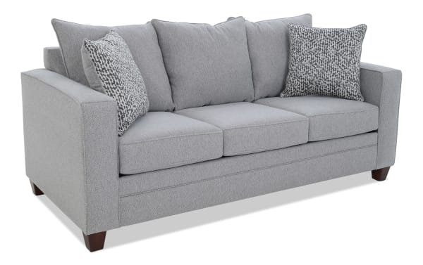 Modern gray fabric sofa with three seat cushions, two patterned throw pillows, and wooden legs, ideal for contemporary living rooms.