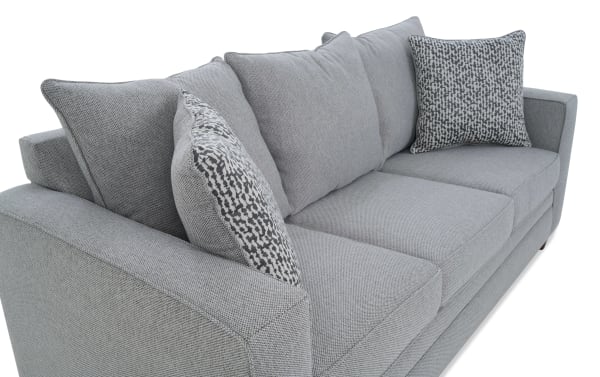 Modern gray fabric sofa with textured upholstery, three large cushions, and two patterned accent pillows, featuring a clean, contemporary design.