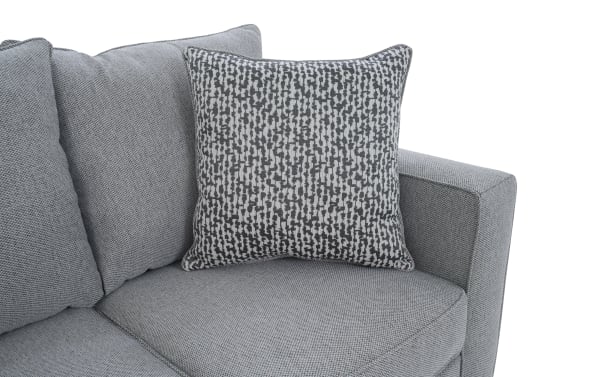 Gray fabric sectional sofa corner with textured gray and white patterned square throw pillow, modern living room furniture design.