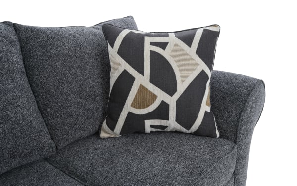 Dark gray fabric sofa corner with a textured black, beige, and brown geometric patterned throw pillow, showcasing modern living room decor.