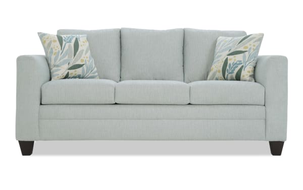 Light blue fabric sofa with three seat cushions, three back cushions, dark wooden legs, and two decorative floral-patterned throw pillows.