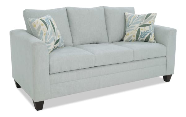 Light blue fabric sofa with three cushioned seats and backrests, featuring two decorative floral-patterned throw pillows and dark wooden legs.