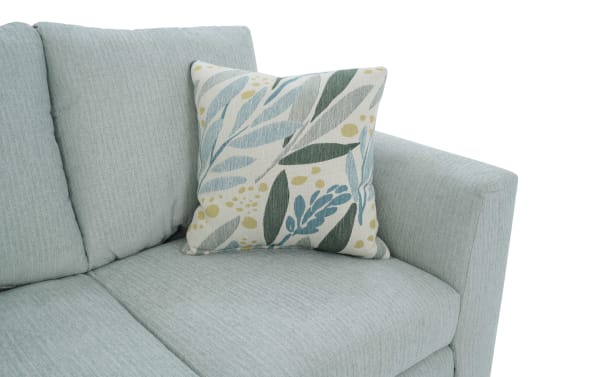 Light blue fabric sofa with a decorative square throw pillow featuring a botanical leaf pattern in shades of green, blue, and beige.
