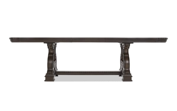 Dark brown wooden dining table with ornate carved pedestal legs and a rectangular top, suitable for formal dining rooms.