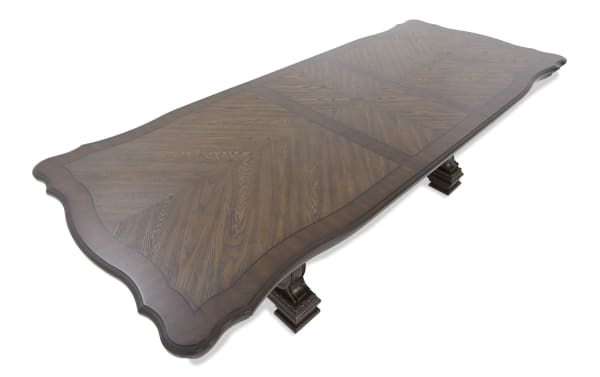 Rectangular dark wood dining table with decorative scalloped edges, detailed wood grain pattern, and two ornate pedestal legs.