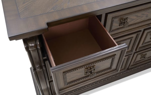 Dark wood desk drawer with ornate carved details and antique brass handle, showcasing smooth finish and spacious interior.
