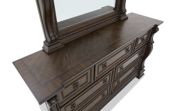 Dark wood dresser with ornate carved details, multiple drawers with antique brass handles, and a matching framed mirror, showcasing classic craftsmanship.