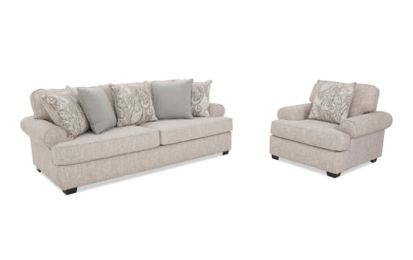 Beige fabric sofa and armchair set with rolled arms and patterned throw pillows, featuring a soft textured upholstery and dark wooden legs.
