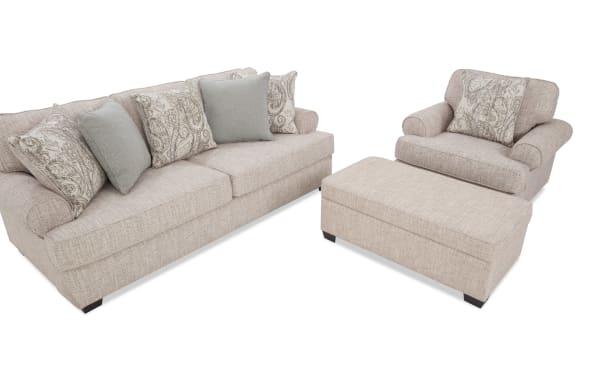 Beige fabric living room set featuring a three-seater sofa, armchair, and matching ottoman with patterned and solid throw pillows, showcasing a cozy, modern style.
