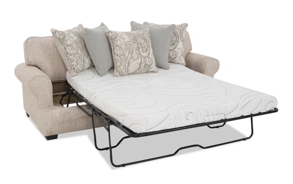 Beige fabric sofa bed with a white patterned mattress and decorative beige and gray throw pillows, featuring a fold-out metal frame for sleeping.