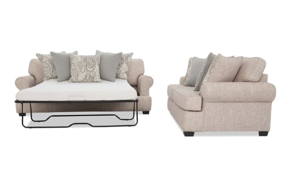 Beige fabric sofa bed with rolled arms, dark wooden legs, and patterned and solid throw pillows, shown open and from side.