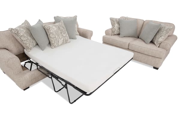 Beige fabric sectional sofa with a pull-out metal frame queen-size sleeper bed, featuring patterned and solid decorative throw pillows.