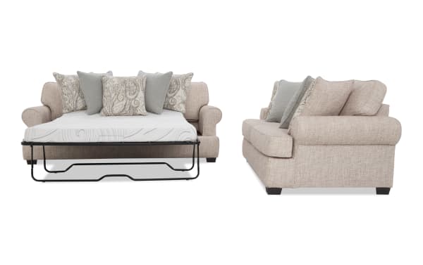 Light beige fabric sofa bed with rolled arms, dark wooden legs, and patterned decorative pillows, shown in open bed position and side view.